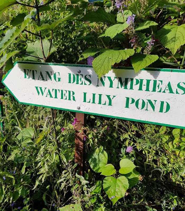 Guide sign leading to Monet’s famous Water Lilies pond in Giverny, surrounded by lush gardens and flowers